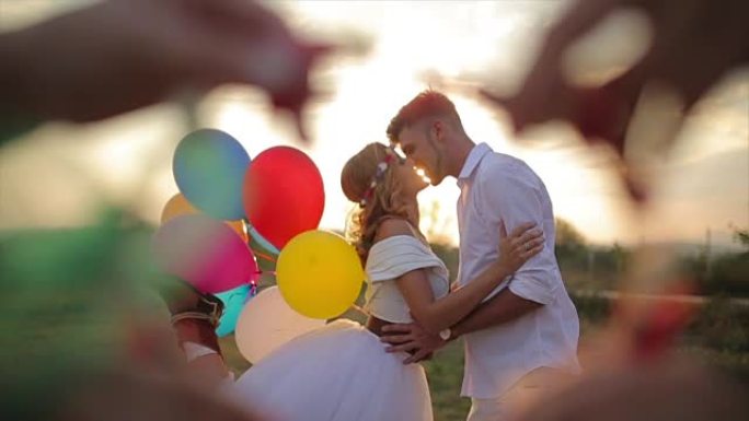 恋爱中的情侣在美丽的日落中亲吻并拿着五彩气球