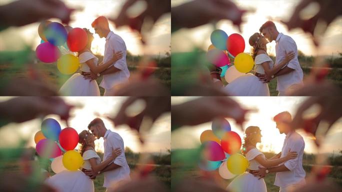 恋爱中的情侣在美丽的日落中亲吻并拿着五彩气球
