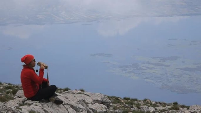 女登山者在湖的背景下从山顶的食堂喝水