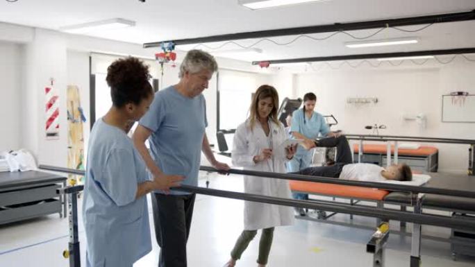 高级男性患者在双杠的帮助下行走，而医生拿着平板电脑和黑人治疗师在他旁边行走