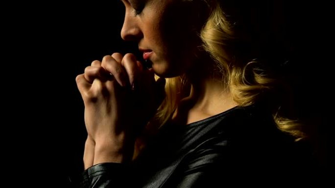 女孩在黑色的孤立祈祷，光落在脸上作为宽恕的标志