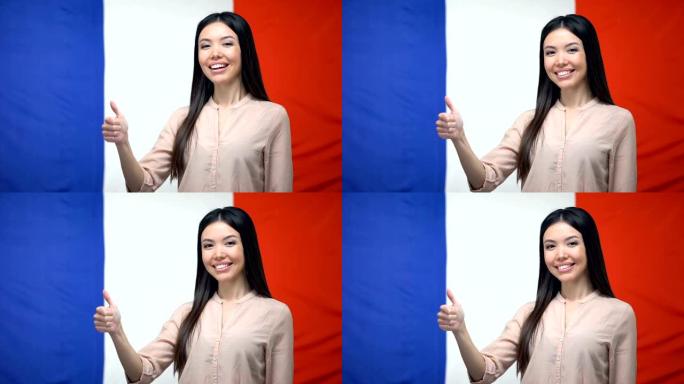 快乐的亚洲女性在法国国旗背景下竖起大拇指，模板