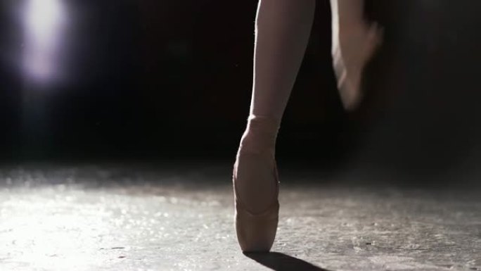 优美的芭蕾舞演员在工作室的黑色背景下，在她的脚尖芭蕾舞鞋上跳舞。女孩穿着脚尖鞋展示经典芭蕾舞剧。框架