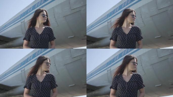 肖像年轻自信的黑发女孩戴着墨镜站在大飞机前。