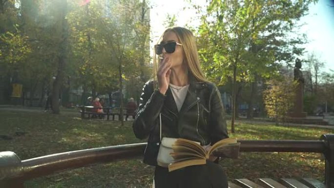 带着书的年轻女子在公园里吸烟