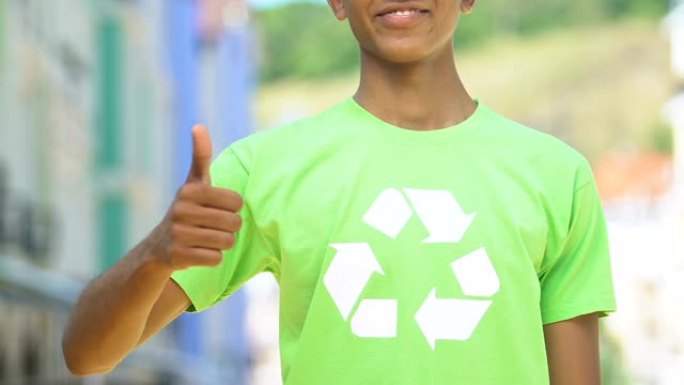 男孩穿着绿色衬衫，上面有回收标志，竖起大拇指表示环保