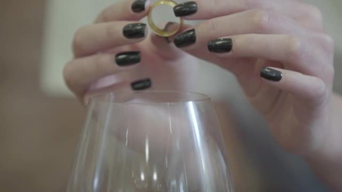 女性双手在白葡萄酒的杯子下握着金色的结婚戒指。