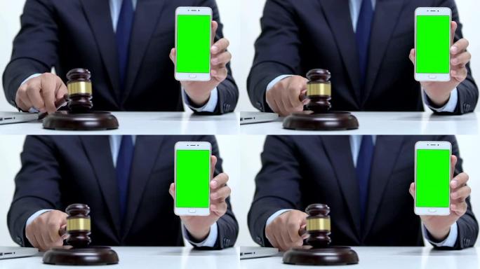 男性拿着绿色屏幕的智能手机，敲击木槌，进行网络犯罪