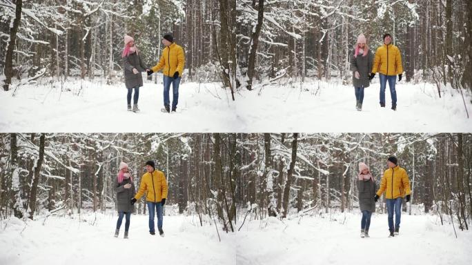 一个穿着黄色夹克的男人和一个戴着帽子和围巾的女孩在降雪期间穿过冬季森林，在圣诞节慢动作中互相笑着微笑