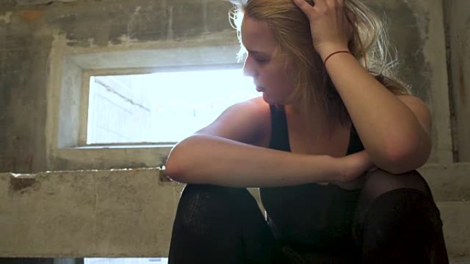 年轻不快乐的女孩坐在一栋废弃建筑的楼梯上