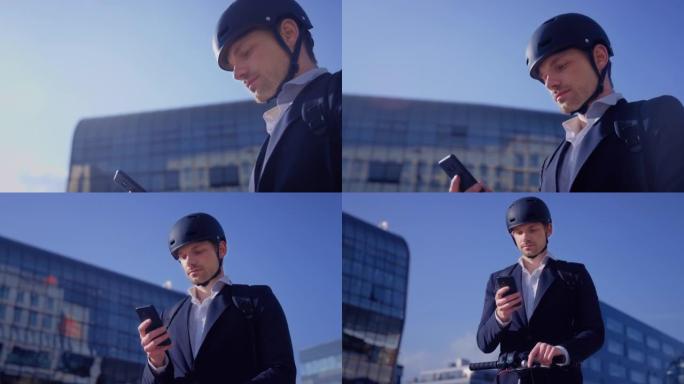 年轻的商人站在他的电动滑板车旁边，在阳光明媚的城市检查他的智能手机
