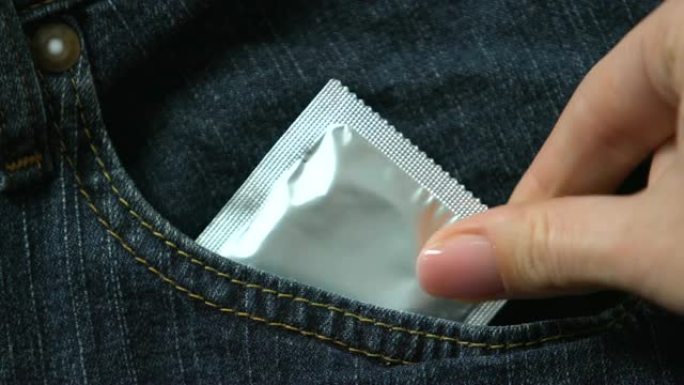 女性手将避孕套放在裤子里，避孕预防怀孕和性传播疾病