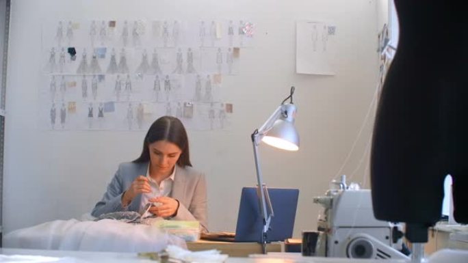 一位年轻的女设计师穿着工作室的连衣裙。裁缝工作室缝纫珠子和珠宝。女裁缝在工作室装饰一件衣服