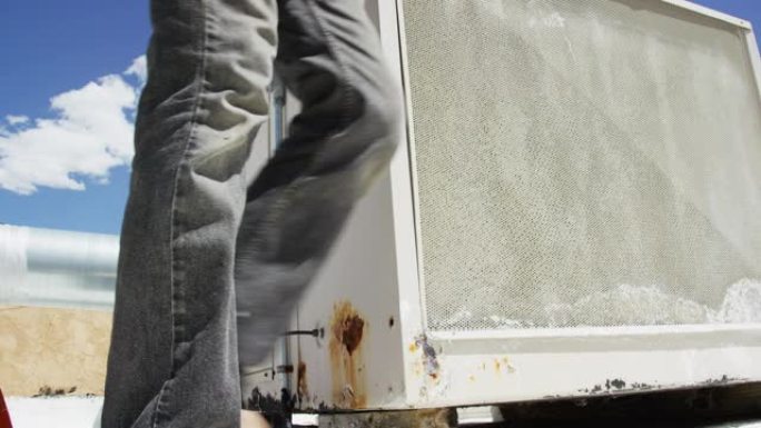 四十多岁的高加索杂工使用可调扳手拧紧屋顶沼泽冷却器外部的连接，然后卸下其中一个屏幕并检查冷却垫，同时