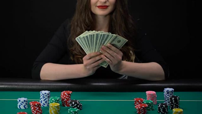 快乐的女人捧着一堆美元，坐在赌桌上，游戏赢家，成功