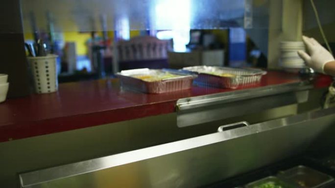 一家墨西哥餐厅的厨师在服务窗口中放置了两个金属烤盘玉米粉蒸肉，并按了铃铛，一个女服务员用票将食物捡起