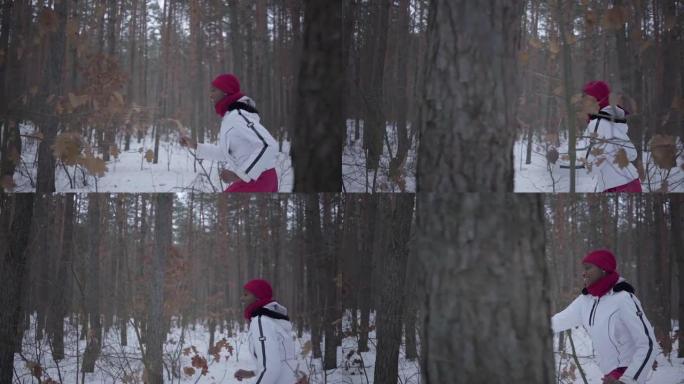 非裔美国女孩穿着暖和的衣服，戴着红色的帽子，围巾和白色的夹克穿过冬季森林。