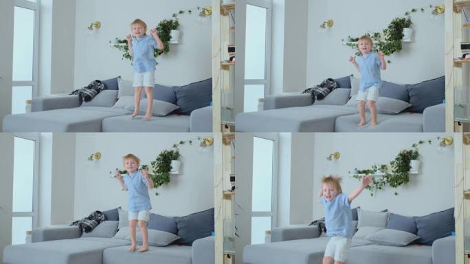 一个4岁的男孩，白色的头发和一件蓝色的衬衫在沙发上跳跃并微笑。有趣和宝贝在家里。恶作剧和纵容