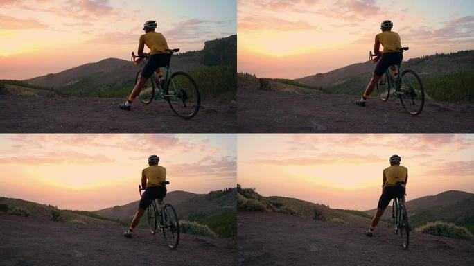 一个穿着骑自行车的人，戴着头盔，坐在公路自行车上，从山顶看日落