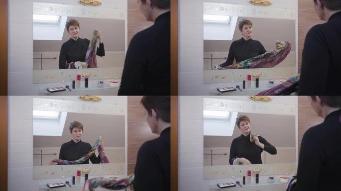 自信的高加索成熟女人站在浴室的大镜子前，尝试五颜六色的围巾。时尚的黑发女商人早上选择服装。风格，时尚