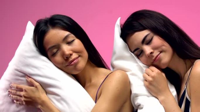 美丽的多民族女性睡在粉红色背景下的枕头上，梦想