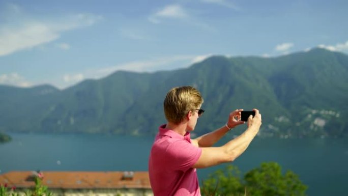 年轻人在山脉和湖泊的视线处用智能手机拍照