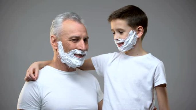 开朗的爷爷和孙子在剃须泡沫中展示剃须刀，男人的仪式