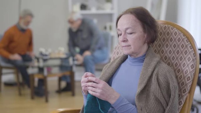 成熟白人妇女检查编织的特写肖像。老年女性退休人员在疗养院练习爱好。