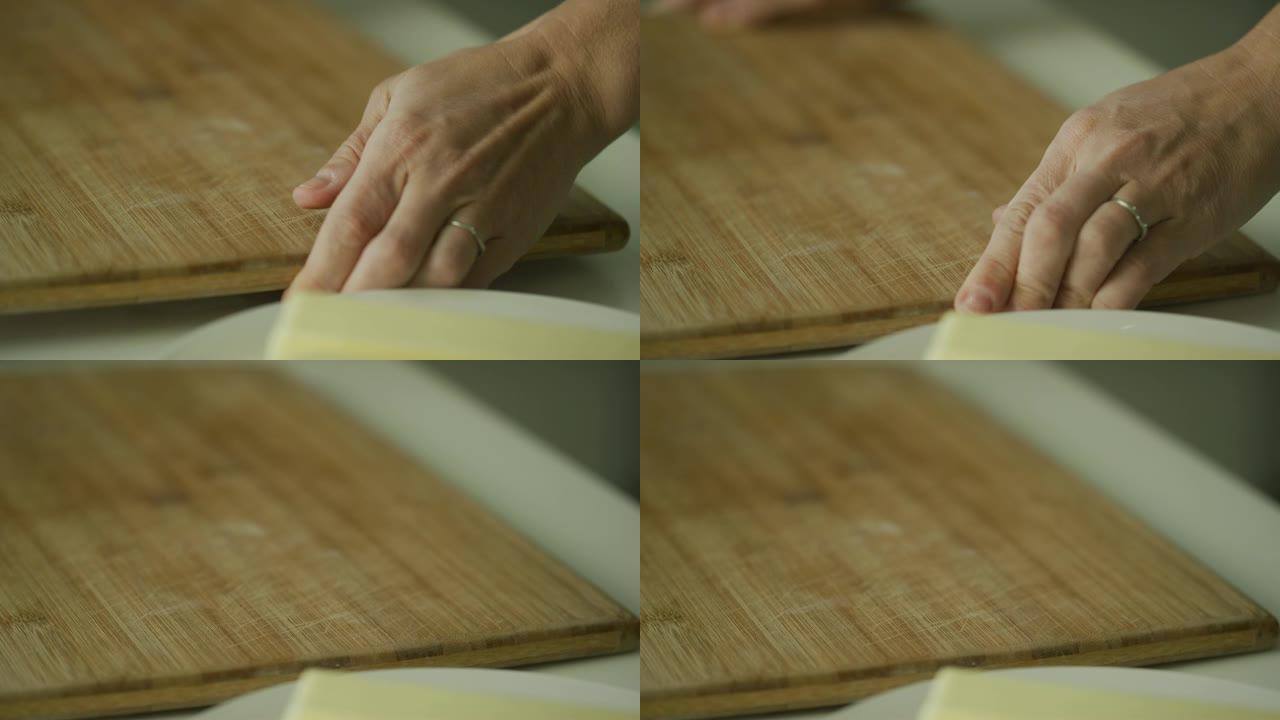 在室内厨房里，一名年轻女子的手在盘子旁边放了一块木板，上面放着两根黄油。