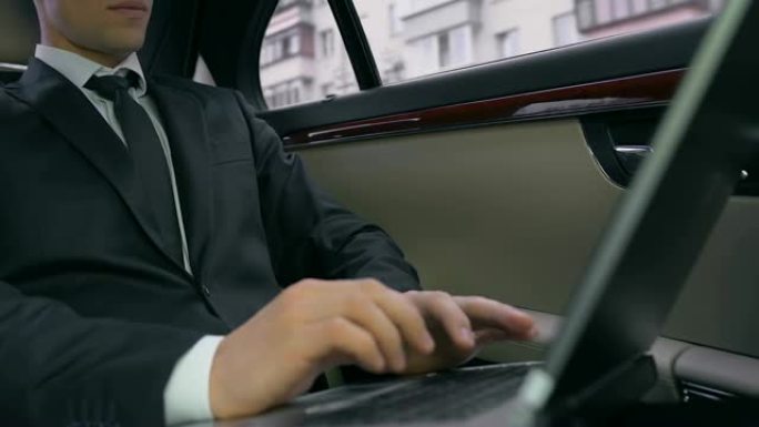 自信的商人坐在汽车后座上，使用笔记本电脑，工作项目
