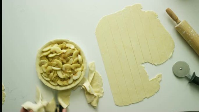 直接用厨房剪刀 (剪刀) 从装满的苹果派上切掉多余的糕点面团，旁边是切成薄片的糕点面团，a面杖和糕点