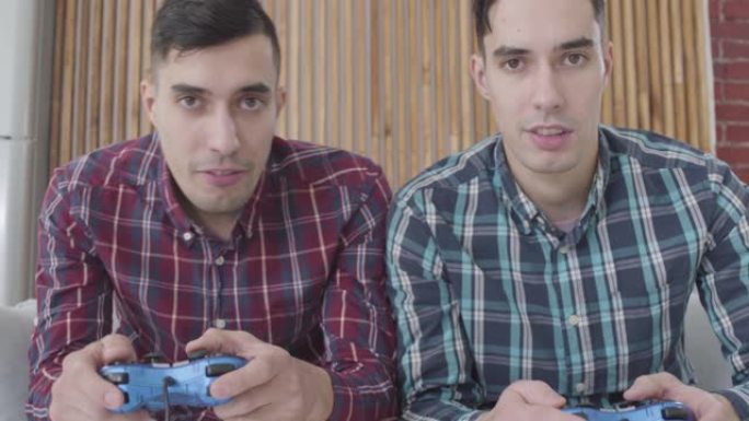 两个同卵双胞胎兄弟看着相机并使用游戏机的特写镜头。快乐的男人在周末玩电子游戏。休闲，快乐，生活方式。