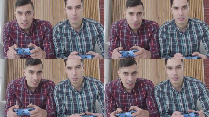 两个同卵双胞胎兄弟看着相机并使用游戏机的特写镜头。快乐的男人在周末玩电子游戏。休闲，快乐，生活方式。