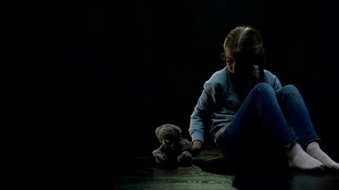 小女孩独自坐在黑暗的房间里拥抱泰迪熊，缺少朋友