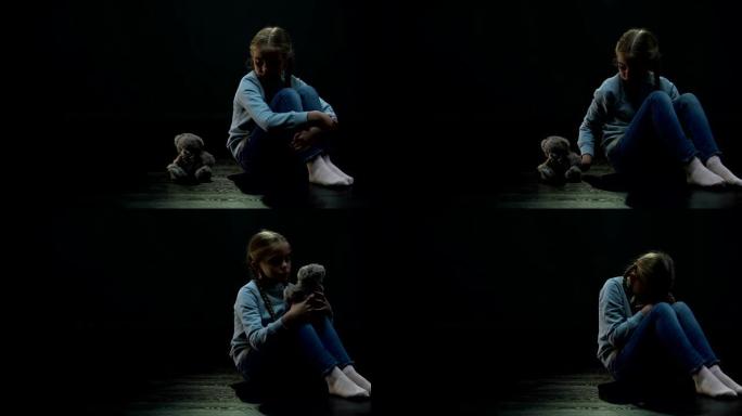 小女孩独自坐在黑暗的房间里拥抱泰迪熊，缺少朋友