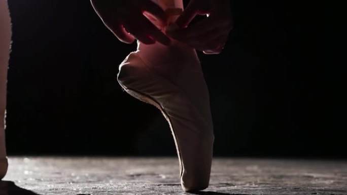 封闭的女性双手系芭蕾舞鞋，孤立在黑色背景上。慢动作。