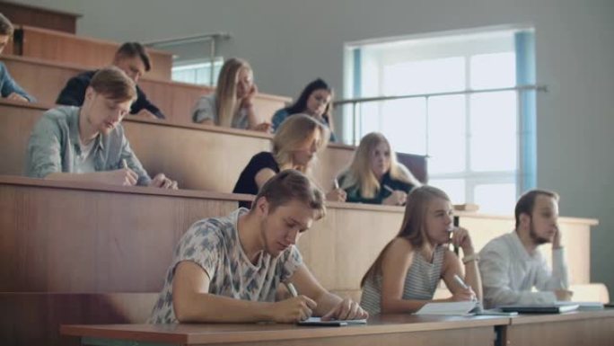 现代学生，无论男女，都坐在大教室的课桌旁，写讲义。