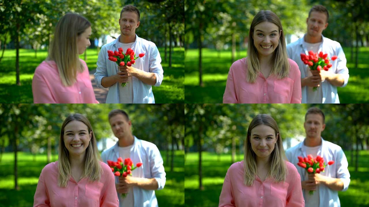 幸福的女人在镜头前微笑，背后有鲜花的男朋友，约会邀请