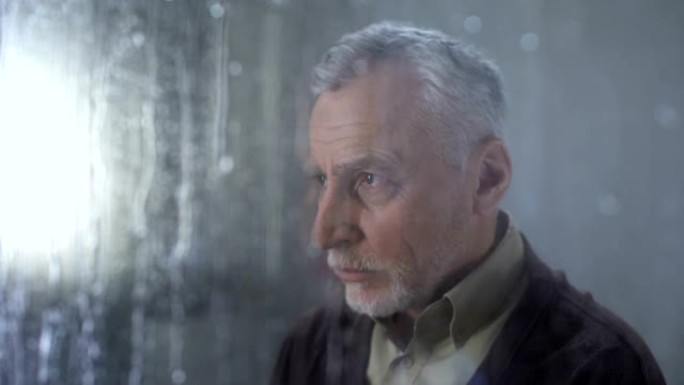 悲伤的男性养老金领取者感到孤独，雨滴窗户玻璃，忧郁，问题