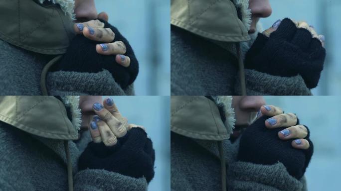 悲惨的无家可归的女人在肮脏的封闭中温暖着她冻结的手，贫穷