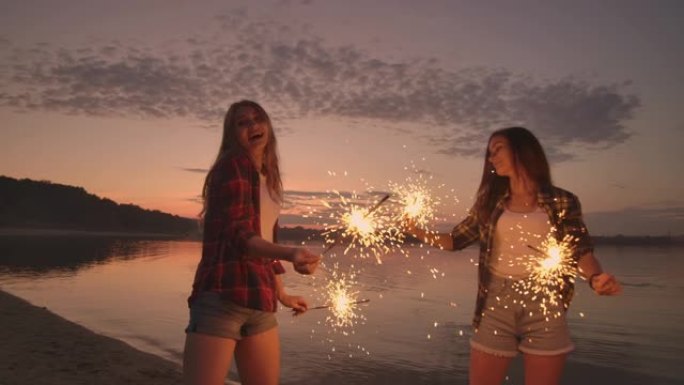 一群朋友的女孩和男人在日落时与慢动作的烟火在沙滩上跳舞。在海滩上庆祝新年。