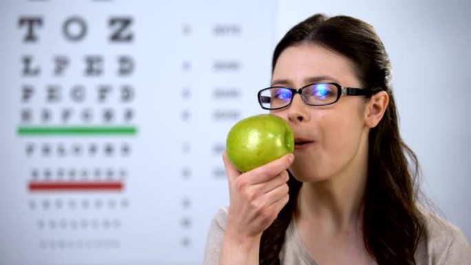 戴着眼镜的微笑女士咬着新鲜的苹果，健康的营养，天然维生素