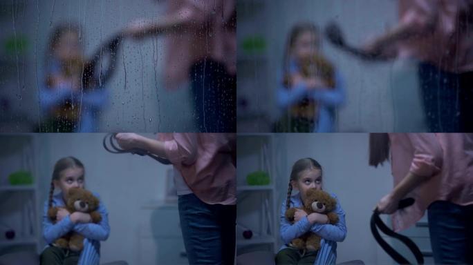 母亲带着皮带威胁女儿在下雨的窗户后面拥抱泰迪熊