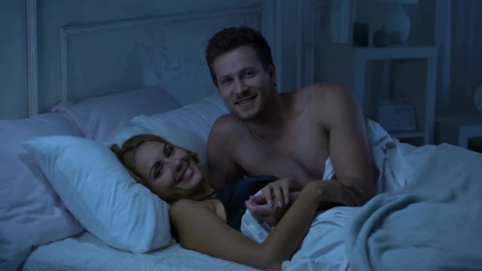 快乐的微笑夫妇躺在床上，看着镜头，解决家庭问题，广告