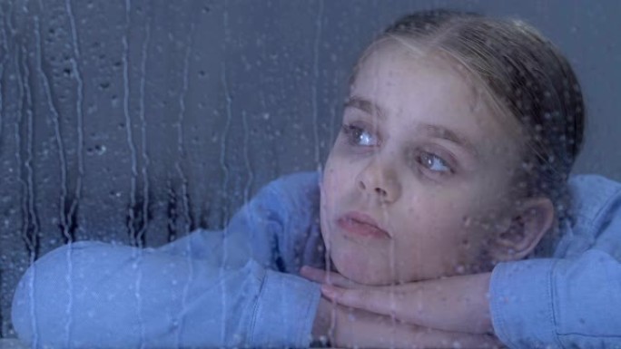 悲伤的女孩在雨滴上看着窗户，梦见孤儿院的家人