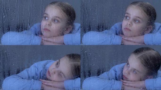 悲伤的女孩在雨滴上看着窗户，梦见孤儿院的家人