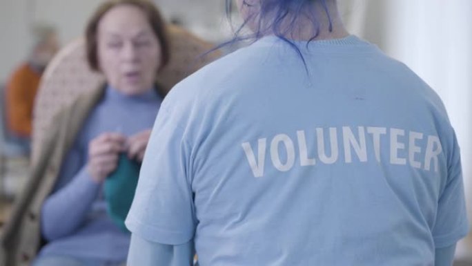 无法辨认的高加索志愿者在疗养院与模糊的老妇人交谈。年轻女孩志愿服务和退休人员聊天的背景图。