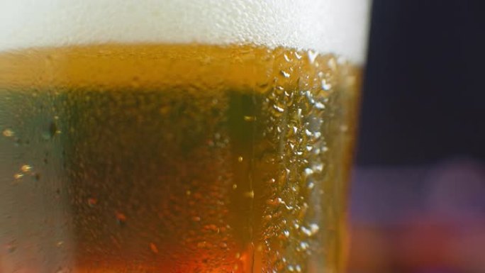 一滴啤酒在一杯啤酒上的微距镜头。一杯冷啤酒上流汗。滴在装满啤酒的玻璃杯上