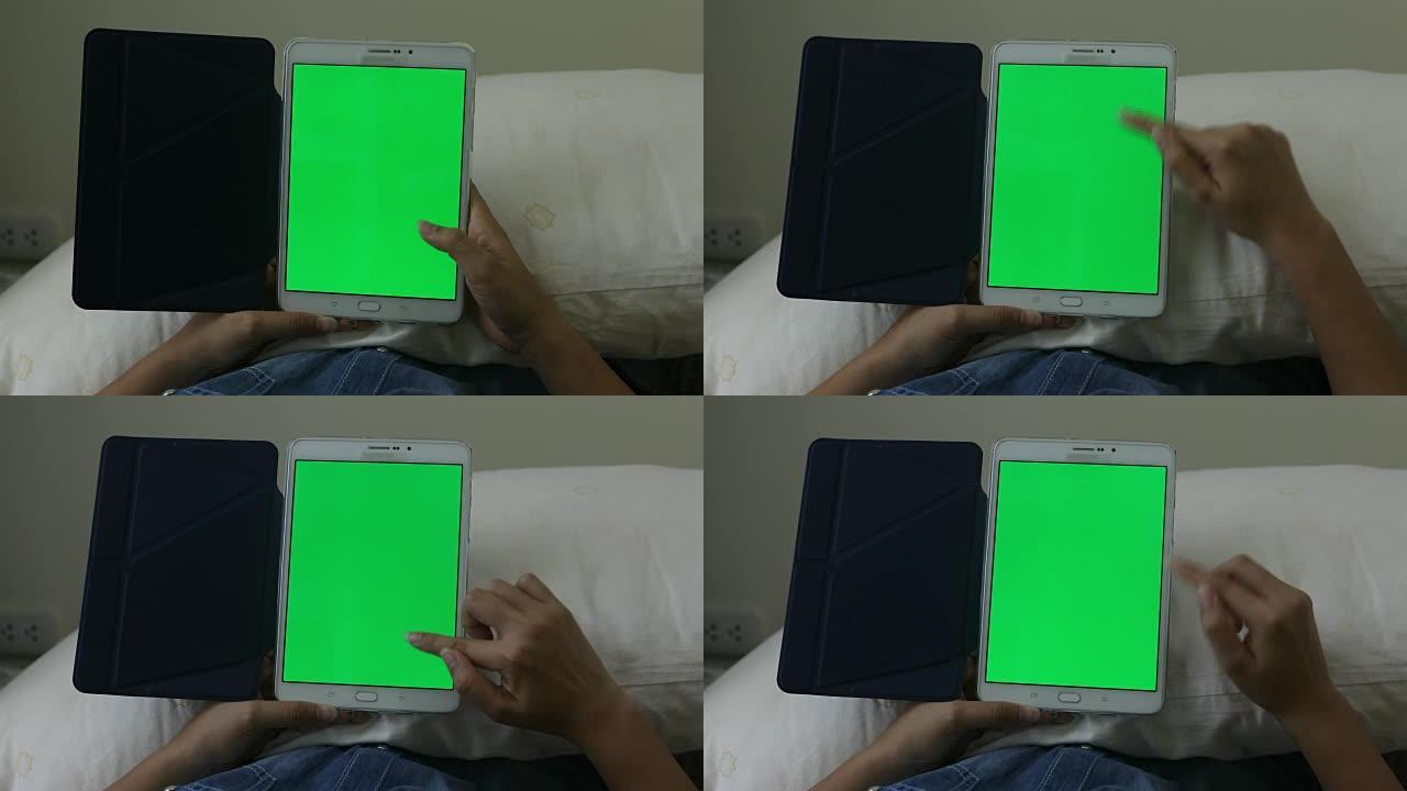 女人坐在床上看着绿屏的平板电脑。用垫子近距离拍摄女人的手