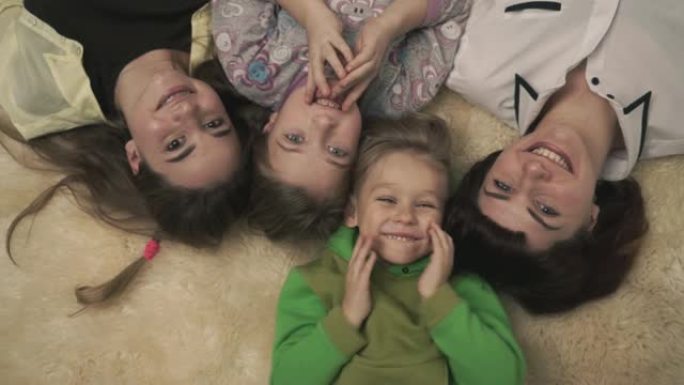 幸福的四口之家的肖像躺在地板上蓬松的地毯上，微笑着。有趣的家庭假期。